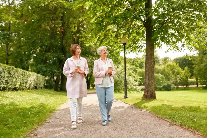 Two senior women walking through a park holding drinks